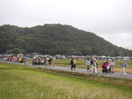 田んぼ道を多くの人が歩いている写真